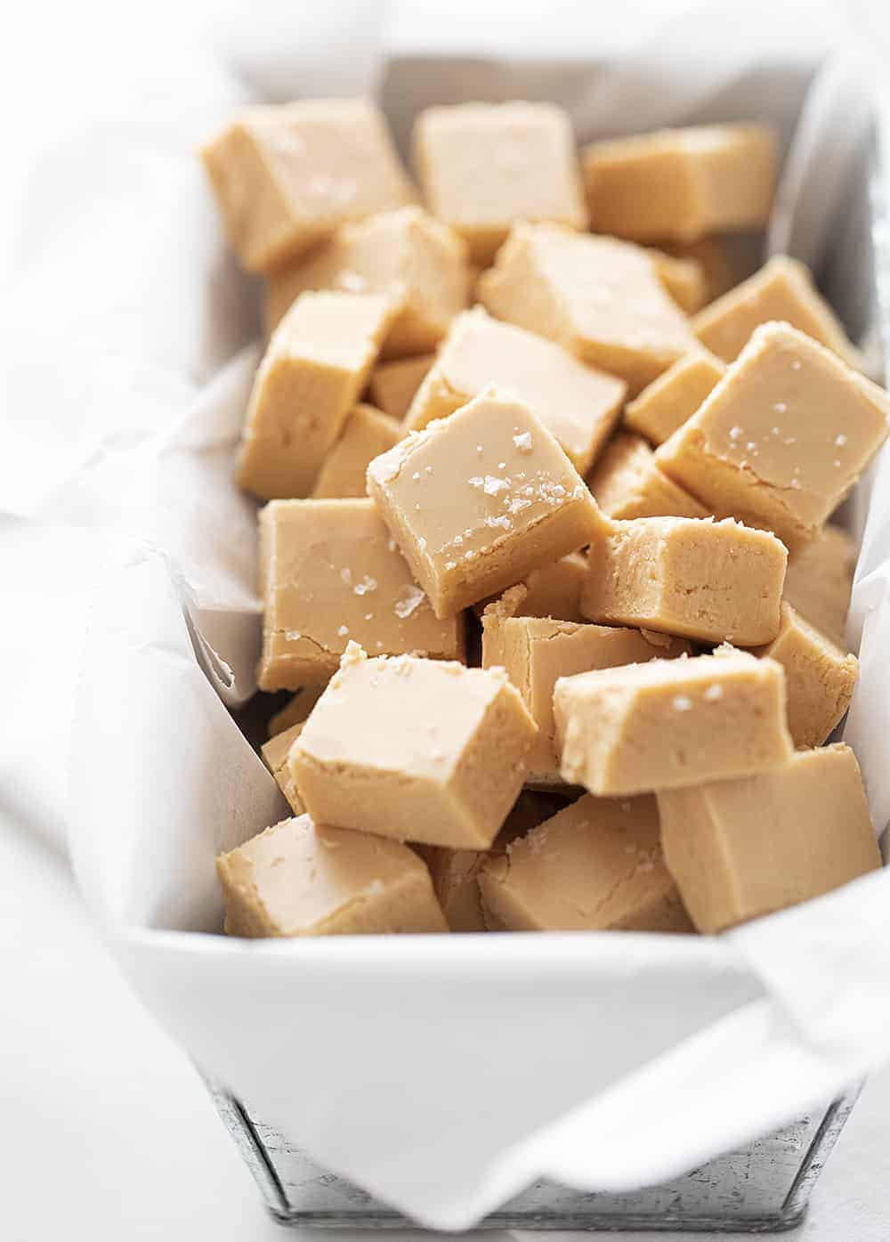 This Salted Caramel Fudge is a smooth and creamy easy caramel fudge with a sea salt topping. Fudge is also perfect for food gifts!! Creamy fudge, fudge recipe, salted caramel fudge, how to make fudge, caramel fudge, caramel fudge recipe, salted caramel fudge recipe, recipes, i am baker Salted Caramel Fudge Cut into Pieces in Metal Container