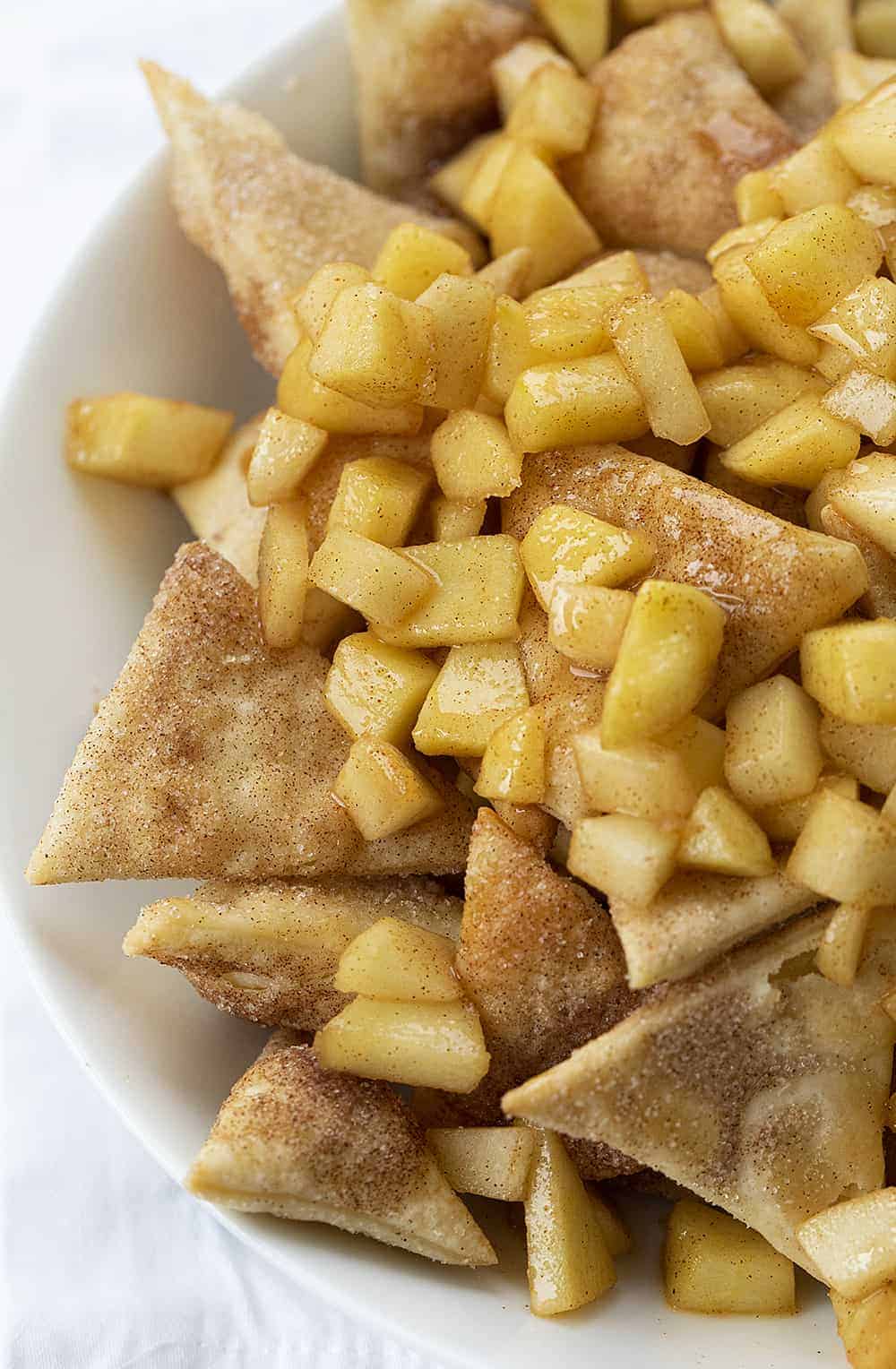Apple Pie Dessert Nachos are homemade cinnamon-sugar chips, topped with sweetened apples, whipped cream, and drizzled with caramel. apple pie dessert nachos, dessert nachos, apple pie nachos, homemade whipped cream, baked cinnamon sugar chips, baking dessert recipes, apple pie, iambaker, i am baker Close Up of Bowl of Apple Pie Nachos on White Napkin