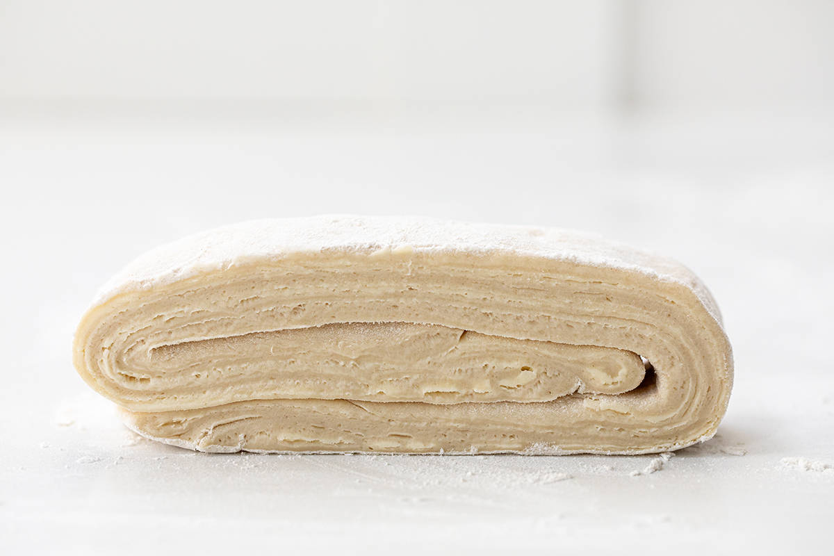 Made entirely from scratch, Homemade Cruffins (croissant + muffin) have buttery, flaky layers with a cinnamon-sugar filling, baked to golden perfection. They are a delightful treat with your morning cup of coffee or tea. Or, enjoy one as a snack or as a dessert! Folded Croissant Dough Before Making From-Scratch Cruffins.