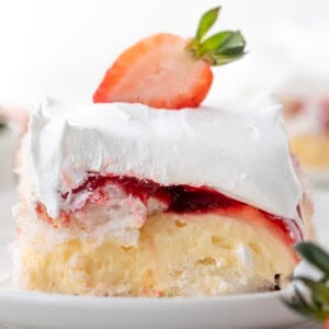 Piece of Strawberry Heaven Dessert on a white plate surrounded by strawberries.