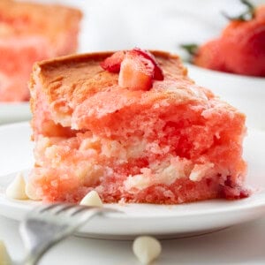 White plate with a piece of Strawberry Earthquake Cake on it and a bite removed with a fork resting on the plate.
