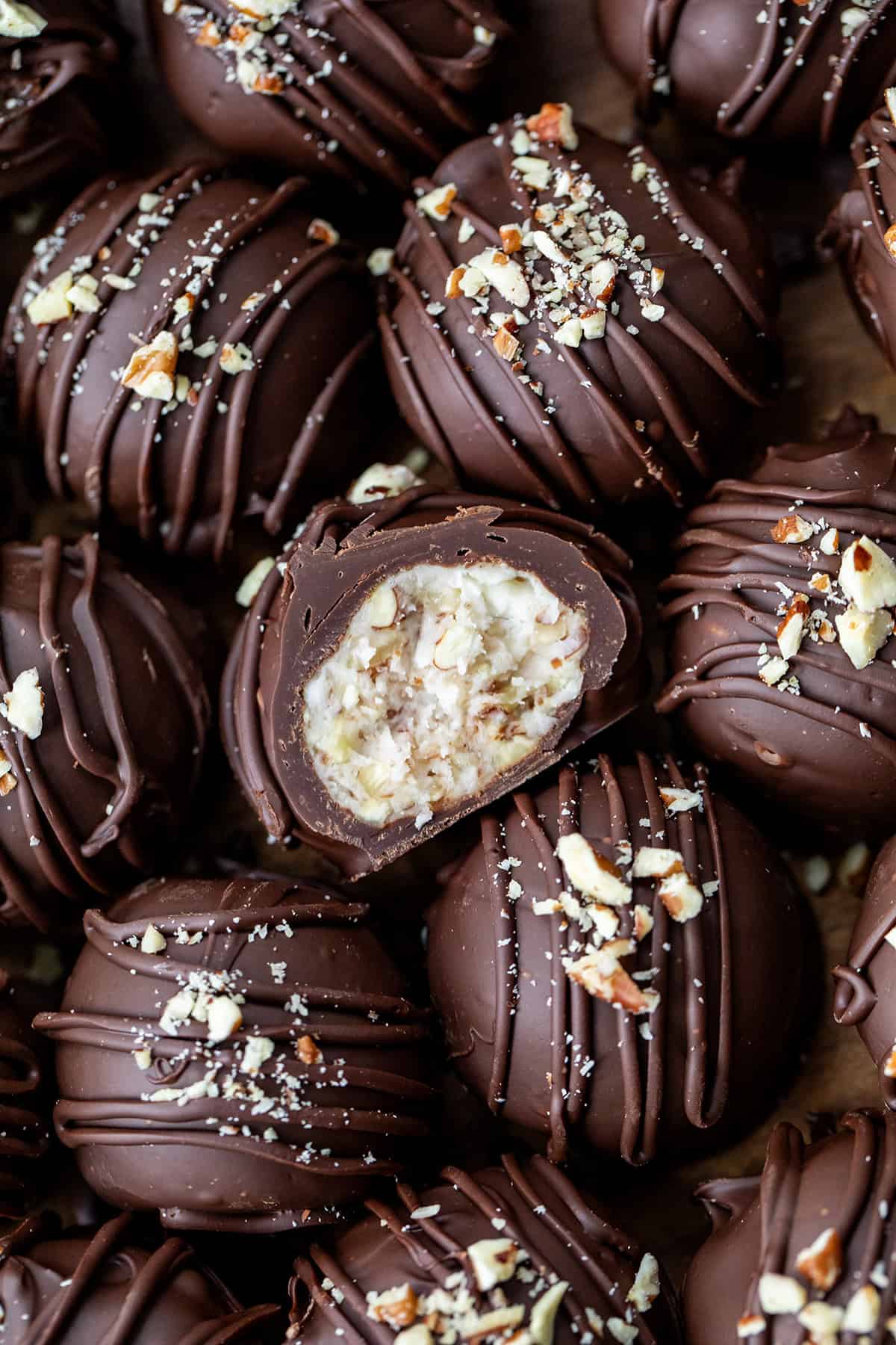 These Bourbon Balls are rich, chocolatey, and packed with a kick of bourbon! With a nutty, creamy center and smooth chocolate shell, theyโre the perfect treat for anyone who loves a boozy dessert! Bourbon Balls very close together and with the center bourbon ball cut in half showing the inside texture.