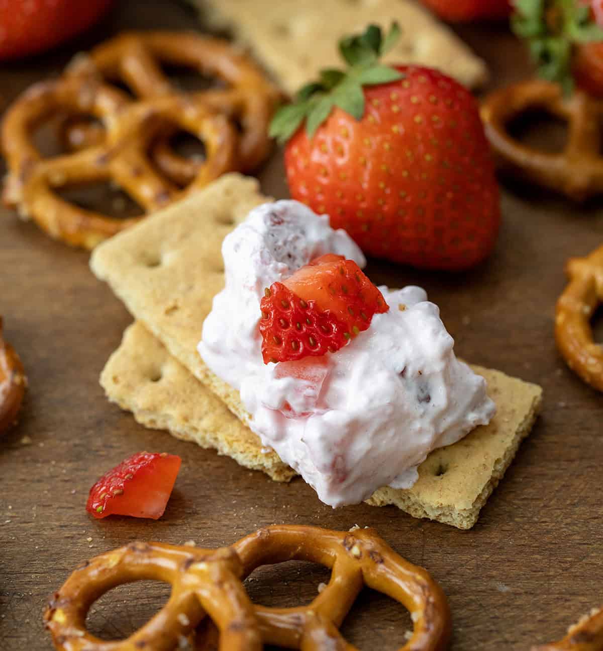 Strawberry Dream Dip is a creamy, dreamy dip that combines cream cheese, whipped topping, strawberry gelatin, and fresh strawberries for a sweet, fruity treat. I love it with graham crackers or pretzels! Graham crackers with Strawberry Dream Dip on it with fresh strawberries and pretzels.