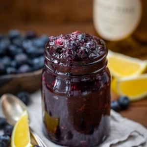 Jar of Blueberry Chardonnay Jam on a wooden table with chardonnay in the background.