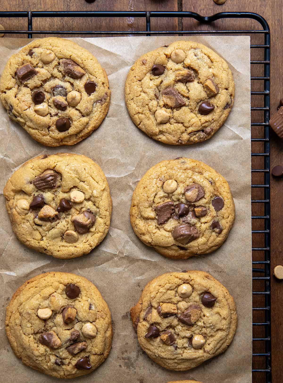 These Reeseโs Peanut Butter Chip Cookies are the ultimate treat for peanut butter and chocolate lovers! Every bite is soft, chewy, and packed with rich, chocolatey, peanut-buttery flavor! Reese's Peanut Butter Chip Cookies on a piece of parchment paper on a cooling rack on a wooden table from overhead.