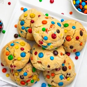 White square platter with Thick and Chewy M&M Cookies on it on a white table from overhead.